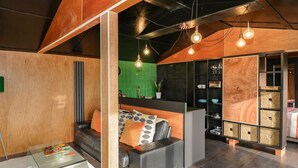 Un intérieur moderne avec un canapé, une table basse en verre et un coin cuisine doté d’étagères et d’un plan de travail.