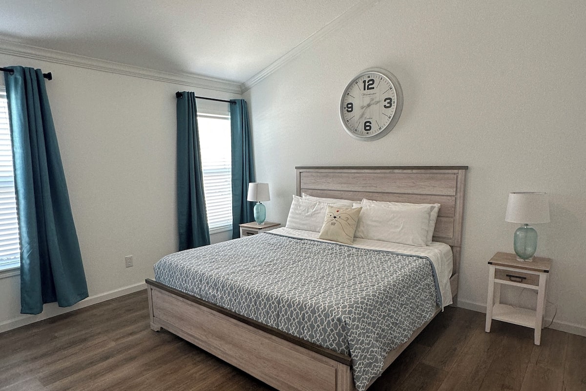 A bedroom with a bed, a ceiling fan, a clock, and a nightstand.