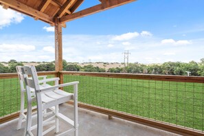 Un balcon avec une chaise blanche, une pergola en bois et une vue sur une pelouse verdoyante et des arbres au loin.