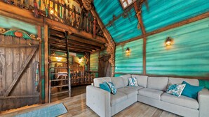 Un interior rústico con una escalera de madera, un sofá grande con cojines estampados y un suelo de madera.
