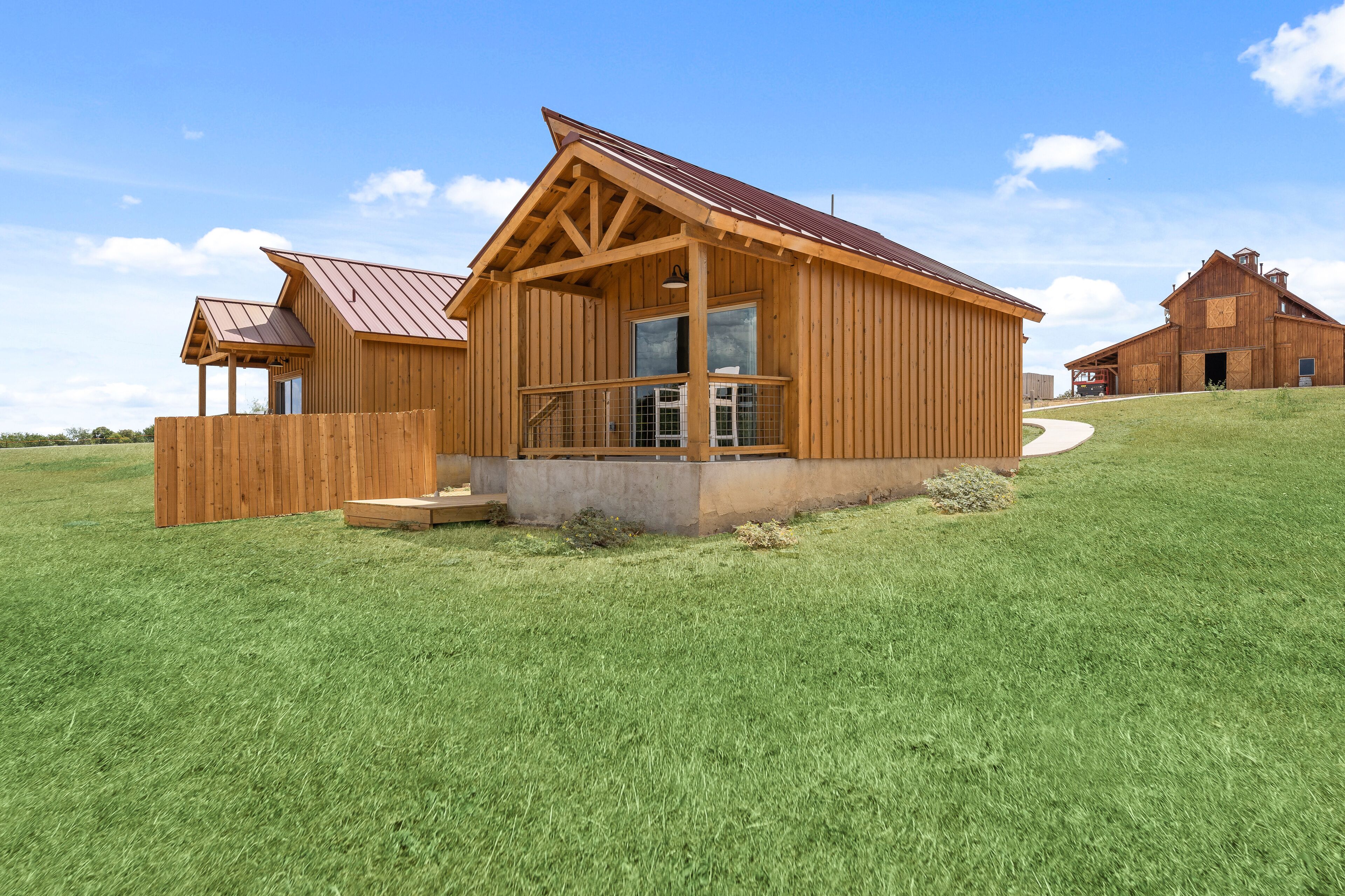 A wooden cabin with a large window and a porch, surrounded by a grassy field.