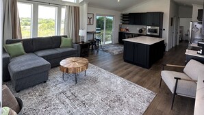 Amplia sala de estar con un sofá grande, una mesa redonda y una cocina con armarios oscuros y una isla central.