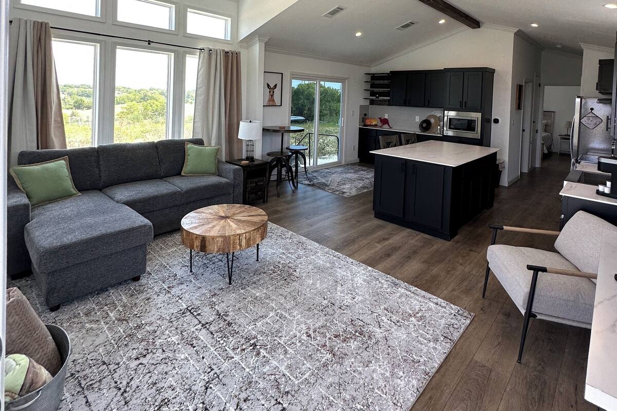 A spacious living area with a large sofa, a round coffee table, and a kitchen with dark cabinetry and a central island.