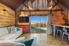 A cozy room with a wooden ceiling, a sofa with cushions, a dining table with chairs, and a large sliding glass door leading to an outdoor area. - Blue Hills Ranch (McGregor)