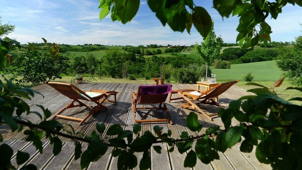 A wooden deck with lounge chairs and a table, overlooking a green landscape with trees and hills. - Les hauts de Saint Christaud: large gite overlooking the Pyrenees (Saint-Christaud)