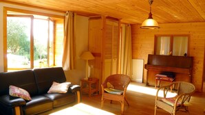 A cozy living room with a wooden interior, a sofa, chairs, a piano, and a television. - Les hauts de Saint Christaud: large gite overlooking the Pyrenees (Saint-Christaud)