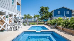 Une piscine divisée en deux zones distinctes, entourée d’une clôture, avec un bâtiment sur la gauche et une maison bleue sur la droite.