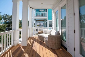 A wooden deck with a white railing, a wicker chair, and a white sofa. - Starfish Shack (Carolina Beach)