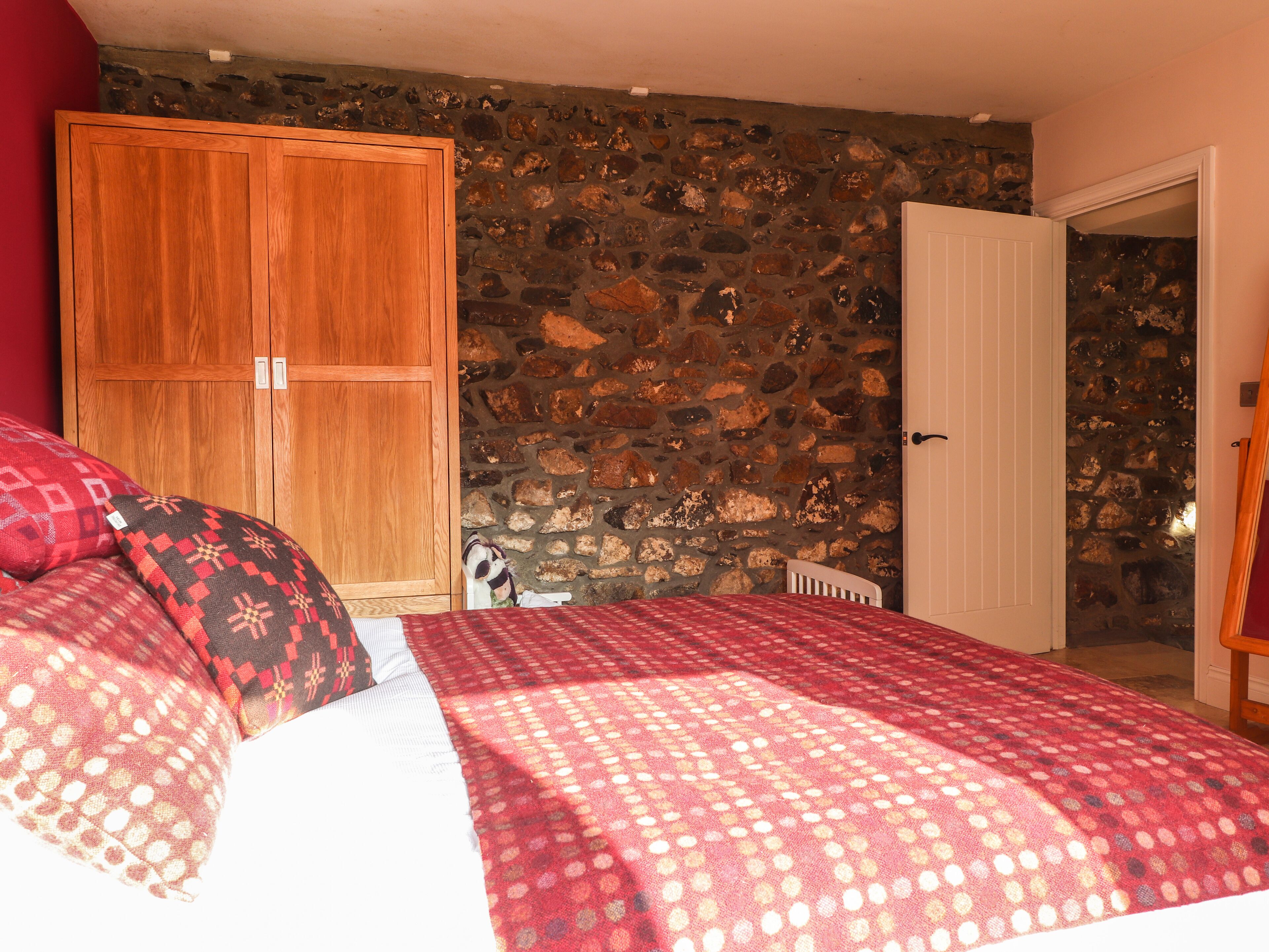 A bedroom with a stone wall, a wooden wardrobe, and a bed with patterned bedding.