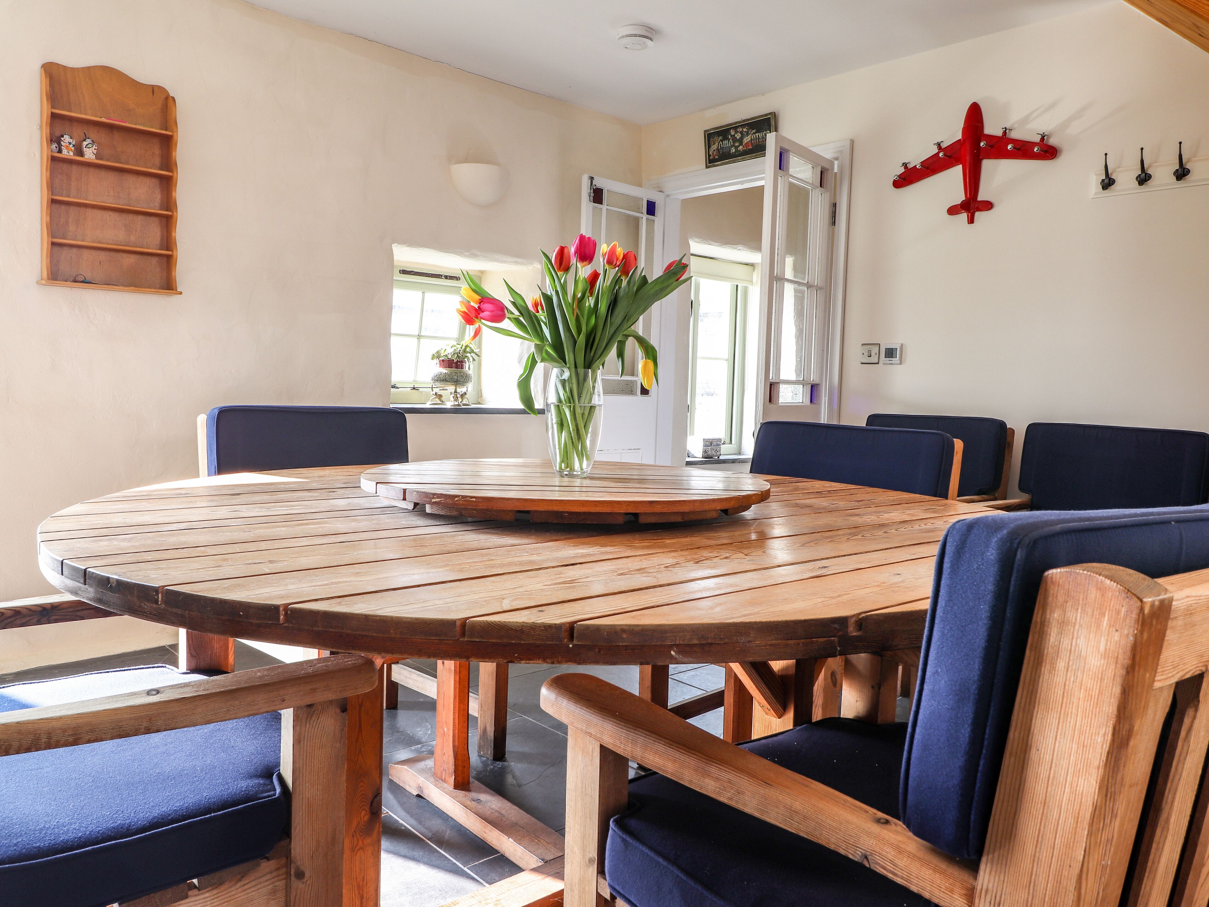 A round wooden table with a central vase of flowers, surrounded by blue upholstered chairs.