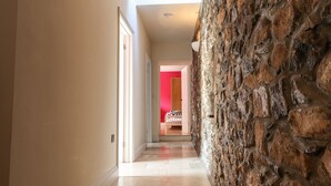A hallway with a stone wall, a door leading to a room with a red wall, and a ceiling light fixture.