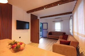 Una sala de estar moderna con una televisión de pantalla plana, techo de madera, sofá y mesa de comedor con fruteros.