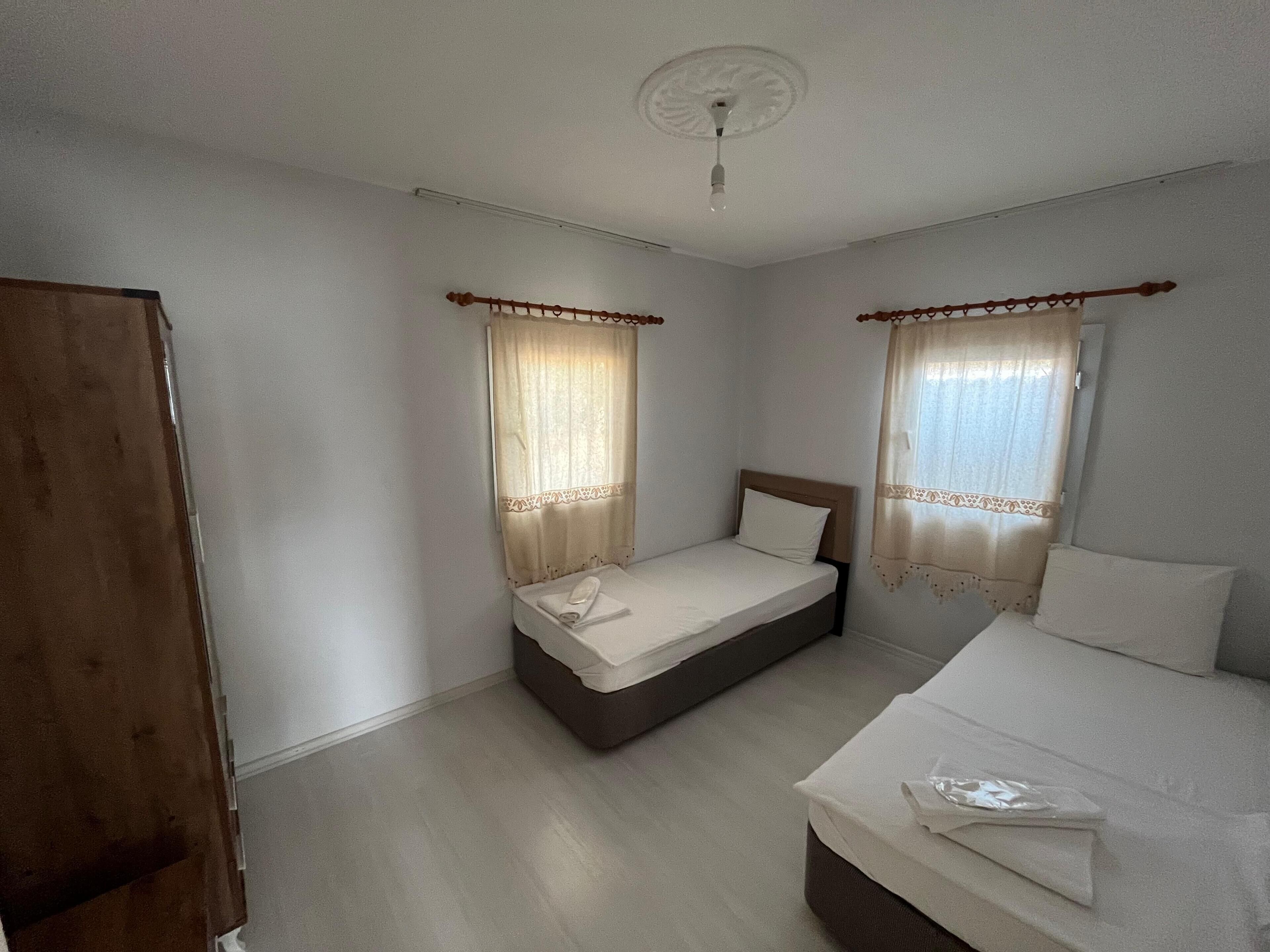 Une petite chambre propre, avec deux lits, une armoire en bois et un ventilateur de plafond.