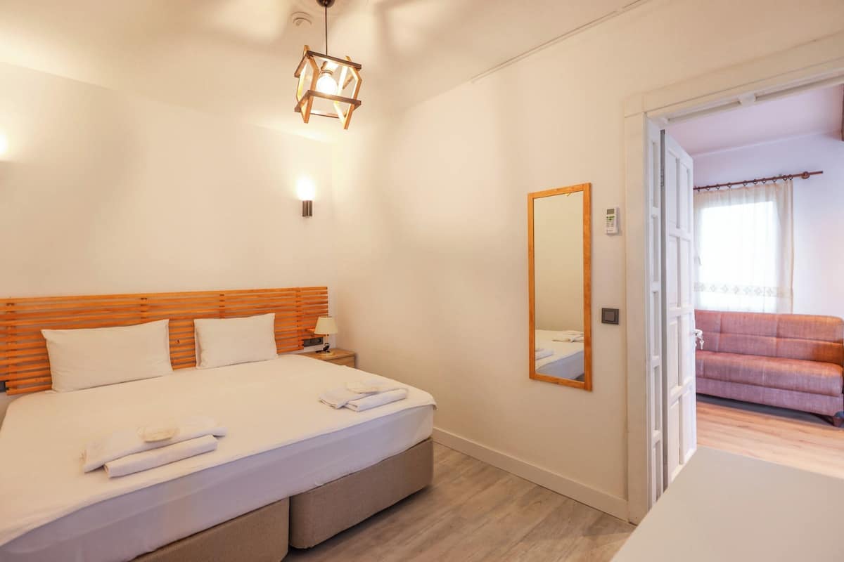 Ein Schlafzimmer mit hölzernem Kopfteil, einem großen Bett mit weißer Bettwäsche, einem Nachttisch mit Lampe und einem Spiegel an der Wand.