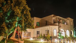 A two-story building with a balcony, a hanging chair, and a well-lit garden at night.