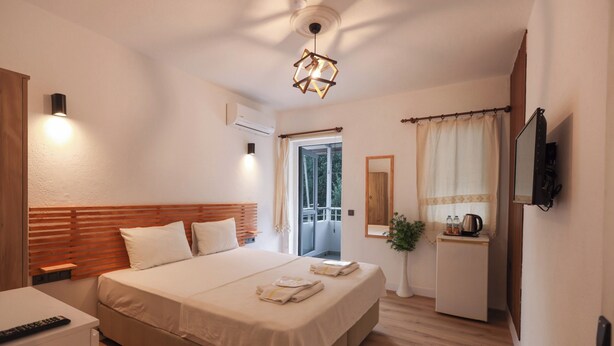A hotel room with a large bed, bedside tables, a TV, a small desk, and a window with curtains.
