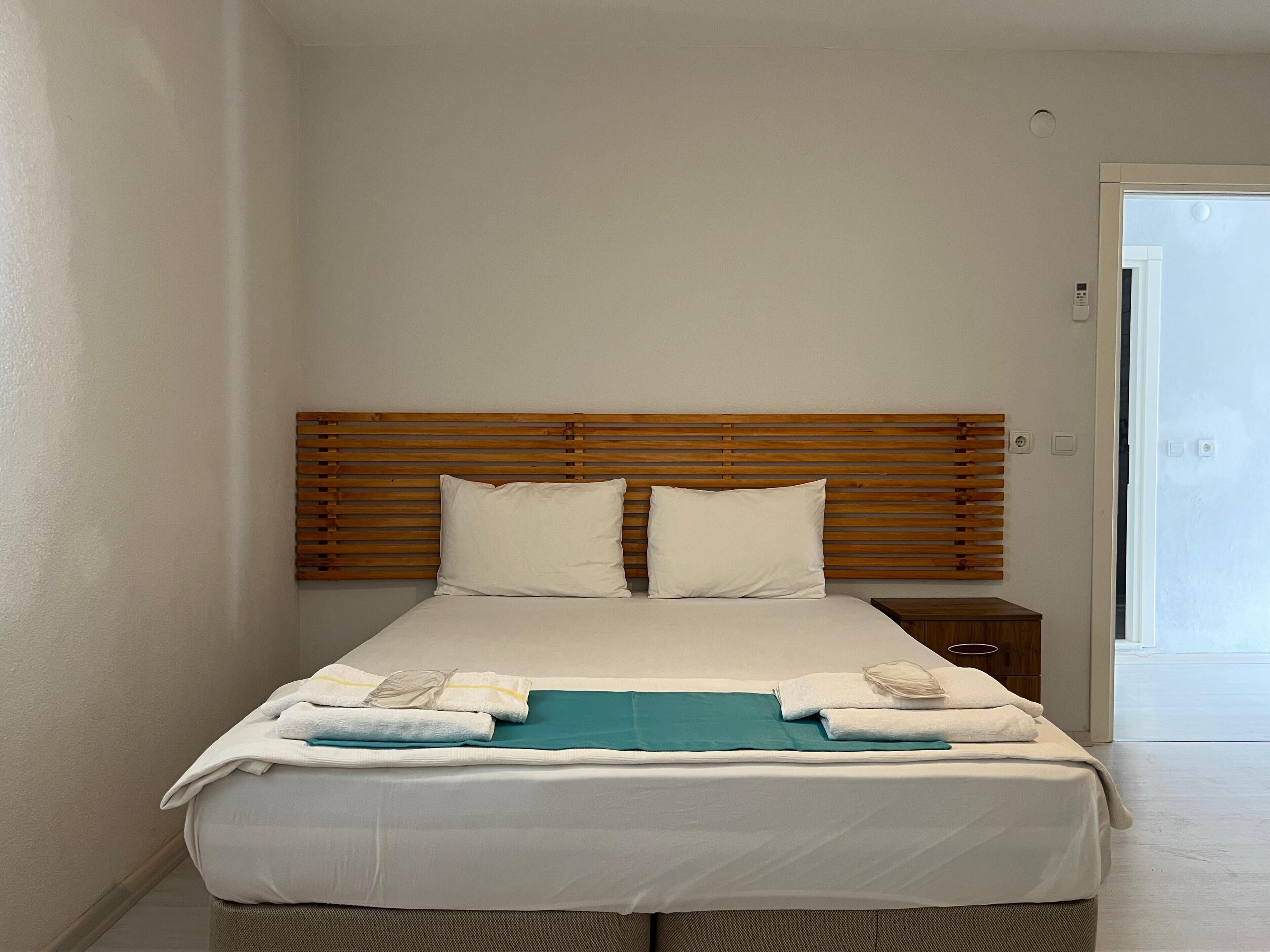 Una cama bien hecha con cabecera de madera, ropa de cama blanca y una manta color turquesa.