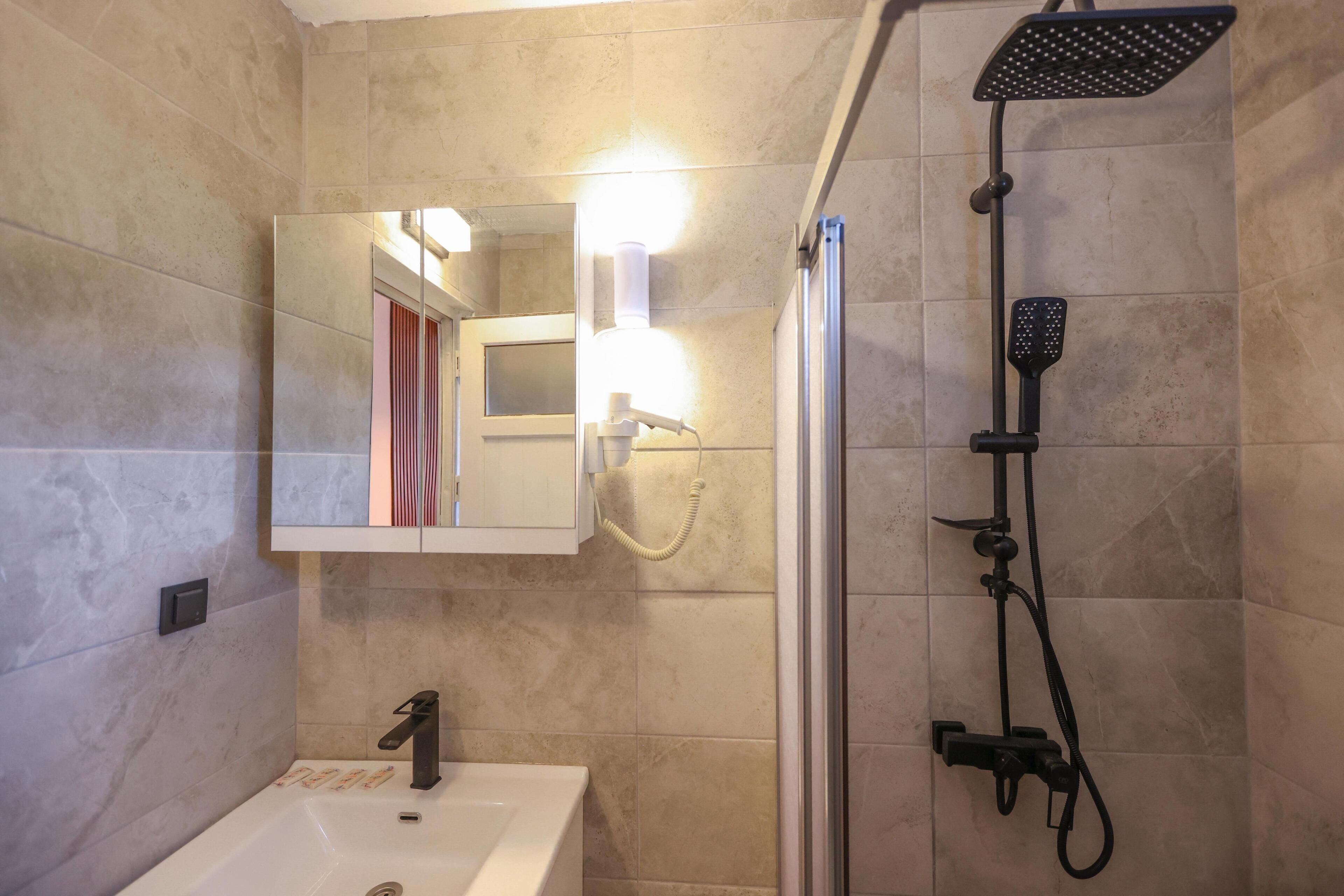 A bathroom with a sink, mirror, shower, and a light fixture.