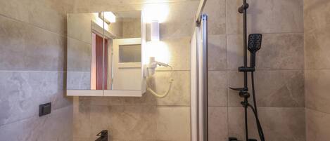 A bathroom with a sink, mirror, shower, and a light fixture.