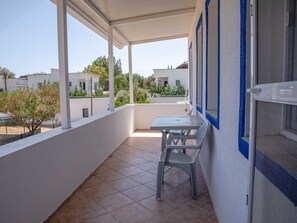 A balcony with a table and chair, white walls, and a view of neighboring buildings and greenery. - Yalıyanı Pansiyon (Bodrum)