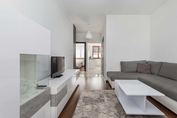 A modern living room with a flat-screen TV, a grey sofa, and a white coffee table.