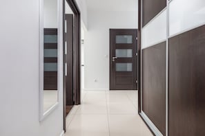 Un pasillo con una puerta de madera, un espejo y suelo de baldosas.