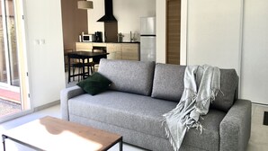 Un salon moderne avec un canapé gris, une table basse en bois et une cuisine en arrière-plan.