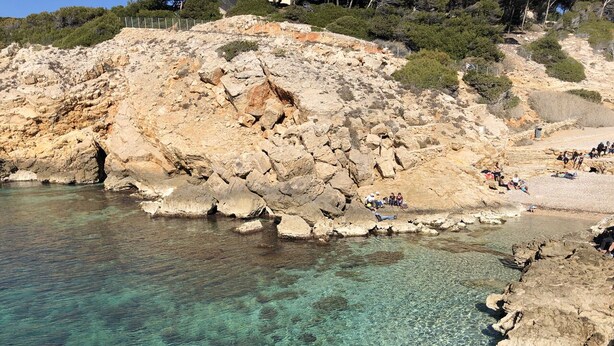 Une zone côtière rocheuse, avec une eau claire et des gens qui se détendent sur la plage.