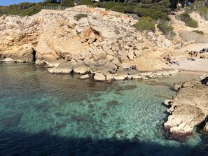 A rocky coastal area with clear water and people relaxing on the shore.