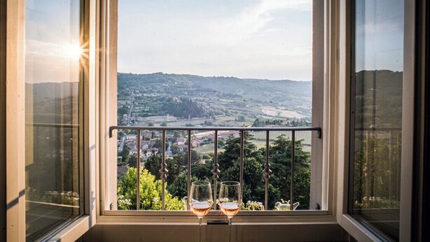 Un balcon avec deux verres à vin, donnant sur un paysage pittoresque composé de collines et d’une ville située en contrebas.