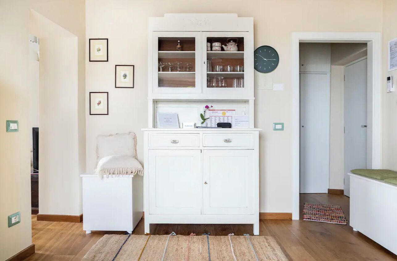 Ein Zimmer mit einem weißen Schrank, einem kleinen Nachttisch, einer Uhr und gerahmten Bildern an der Wand.