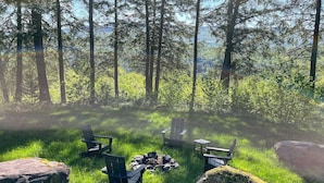 Un campeggio con quattro sedie Adirondack disposte attorno a un braciere centrale, circondato da rocce e vegetazione rigogliosa.