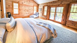 Camera da letto in una baita di legno, con un letto, una sedia e ampie finestre.