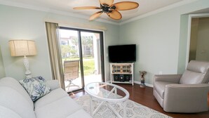 Een woonkamer met een bank, fauteuil, glazen salontafel en een tv-meubel met speakers.