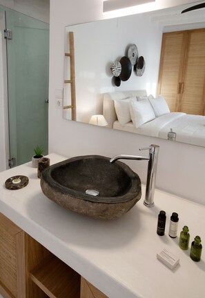 Een moderne badkamer met een groot, rond stenen wastafel, een spiegel en een houten kastje.