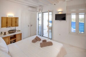A bedroom with a large bed, a wooden vanity, a television, and a view of the sea through the door.