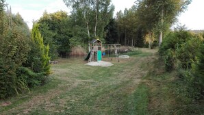 Een speeltuin met een glijbaan en klimconstructie, omringd door weelderige begroeiing.