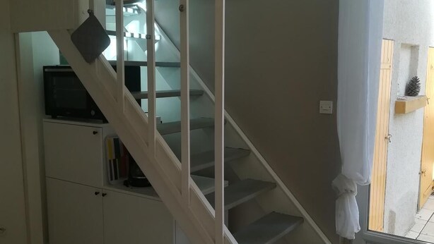 Een trap die uitkomt op een plateau met een magnetron en boeken op een kast, een houten tafel en een mat met een rode pijl op de vloer.