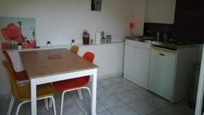 Een compacte keuken met een eethoek, met een houten tafel, rode stoelen en witte kastjes.