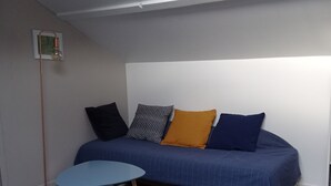 Een kleine, moderne kamer met een blauwe bank, een klein rond tafeltje en een vloerlamp.