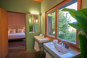Un baño moderno con un ventanal grande, un lavabo doble y una cama con cabecero.
