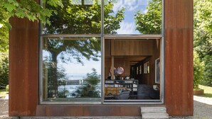 Un edificio moderno con amplios ventanales, interior de madera y vista a un cuerpo de agua.