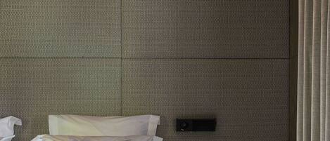 A modern hotel room with a large bed, a bedside table, a lamp, and a wall-mounted control panel.