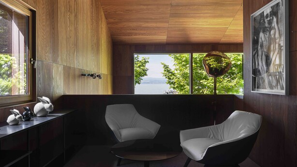 Un interior moderno con dos sillas blancas, techo de madera y vista al exterior.