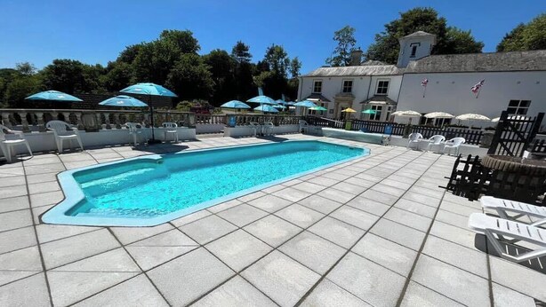 Una piscina rectangular con solárium empedrado, rodeada de sillones de playa y sombrillas.