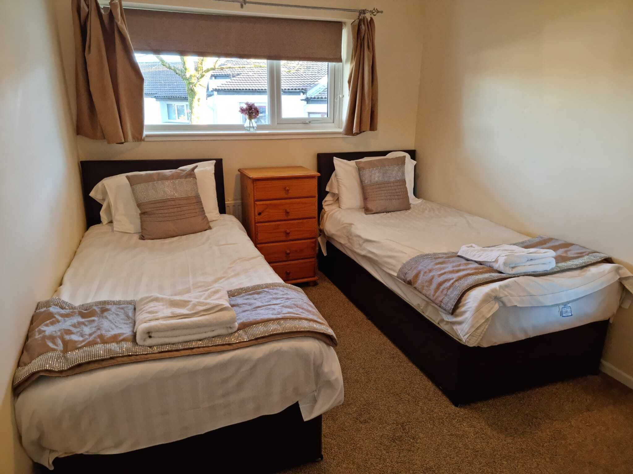 A bedroom with two single beds, a wooden dresser, and a window with curtains.