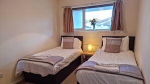 Un dormitorio con dos camas individuales, una mesita de noche con lámpara, una ventana con cortinas y vistas al exterior.