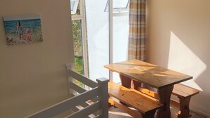 Un salón acogedor con una mesa de madera y bancos, una barandilla blanca y vistas a través de un amplio ventanal.