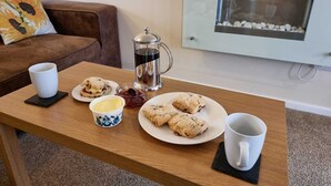 Una mesa de madera con una cafetera, dos platos de scones, una taza de mantequilla y una taza.