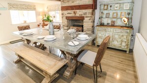 A dining area with a stone fireplace, wooden beams, and a vintage cabinet with framed pictures. - Kingfisher Cottage (Holmfirth)